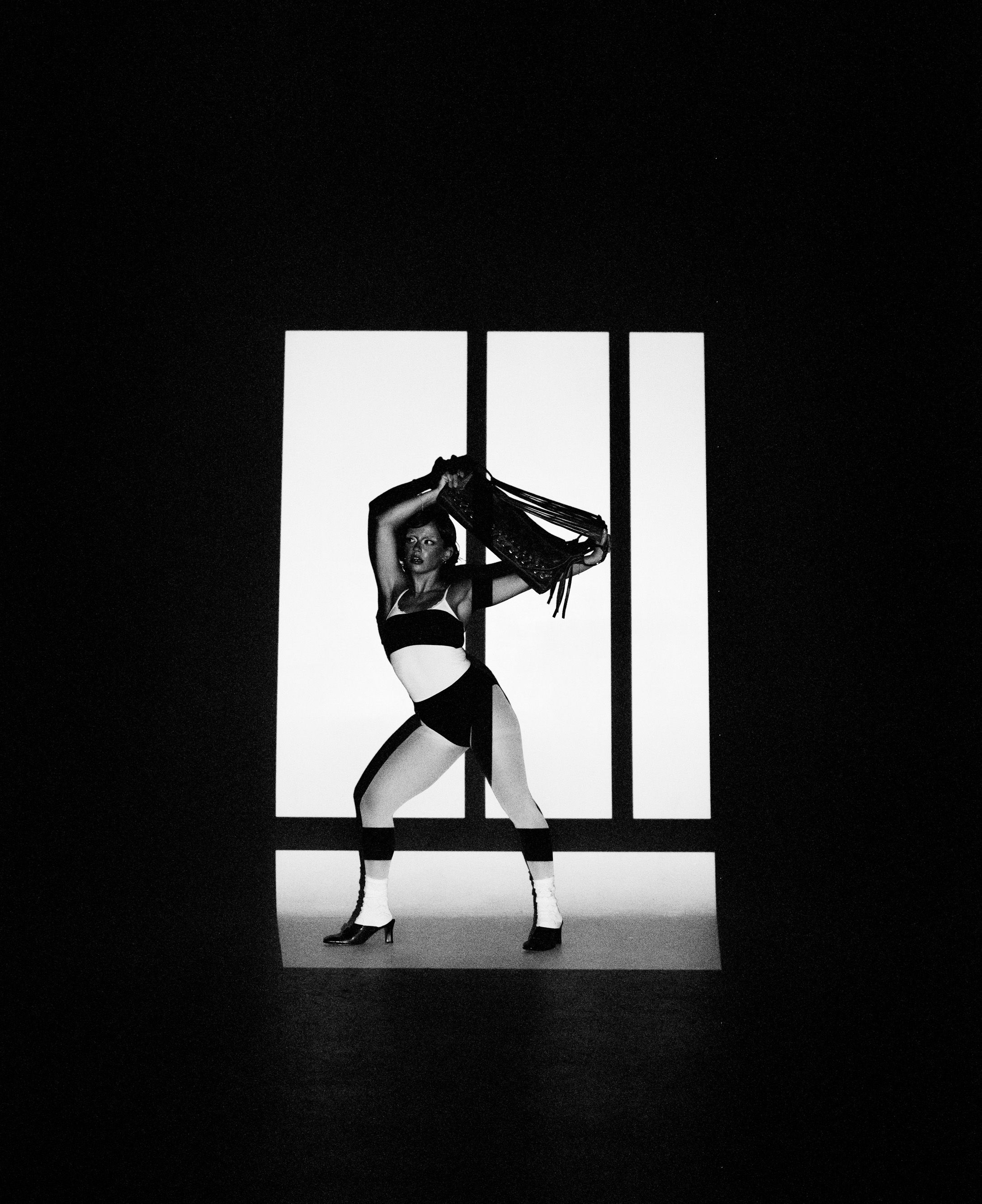 Dynamic pose against white panels creating stark contrast in black and white photography.