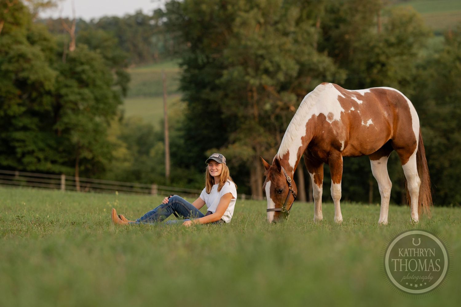 Brown and white patterned horse grazes next to relaxing companion in peaceful countryside setting.