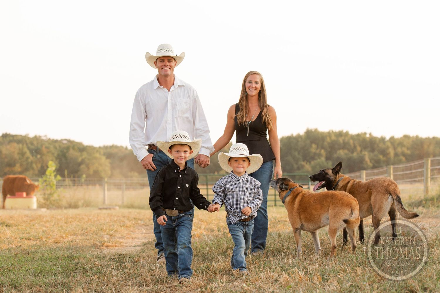 A family walks together on their ranch with cattle grazing in the background.