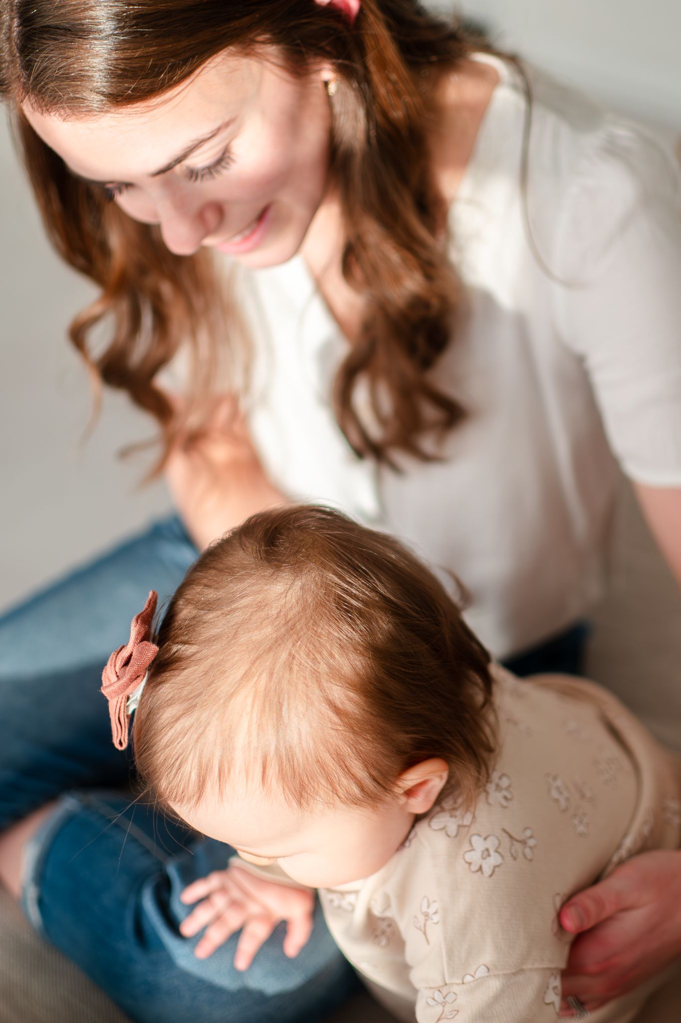 Mother in white blouse sits with baby wearing beige dress in tender loving moment together.