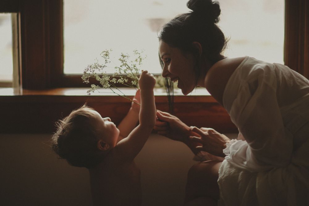 A parent and baby share an intimate bonding moment in soft window light.