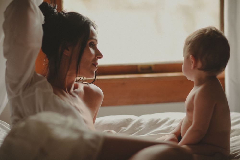 A warm, intimate moment shared between parent and baby sitting together on a bed in soft lighting.