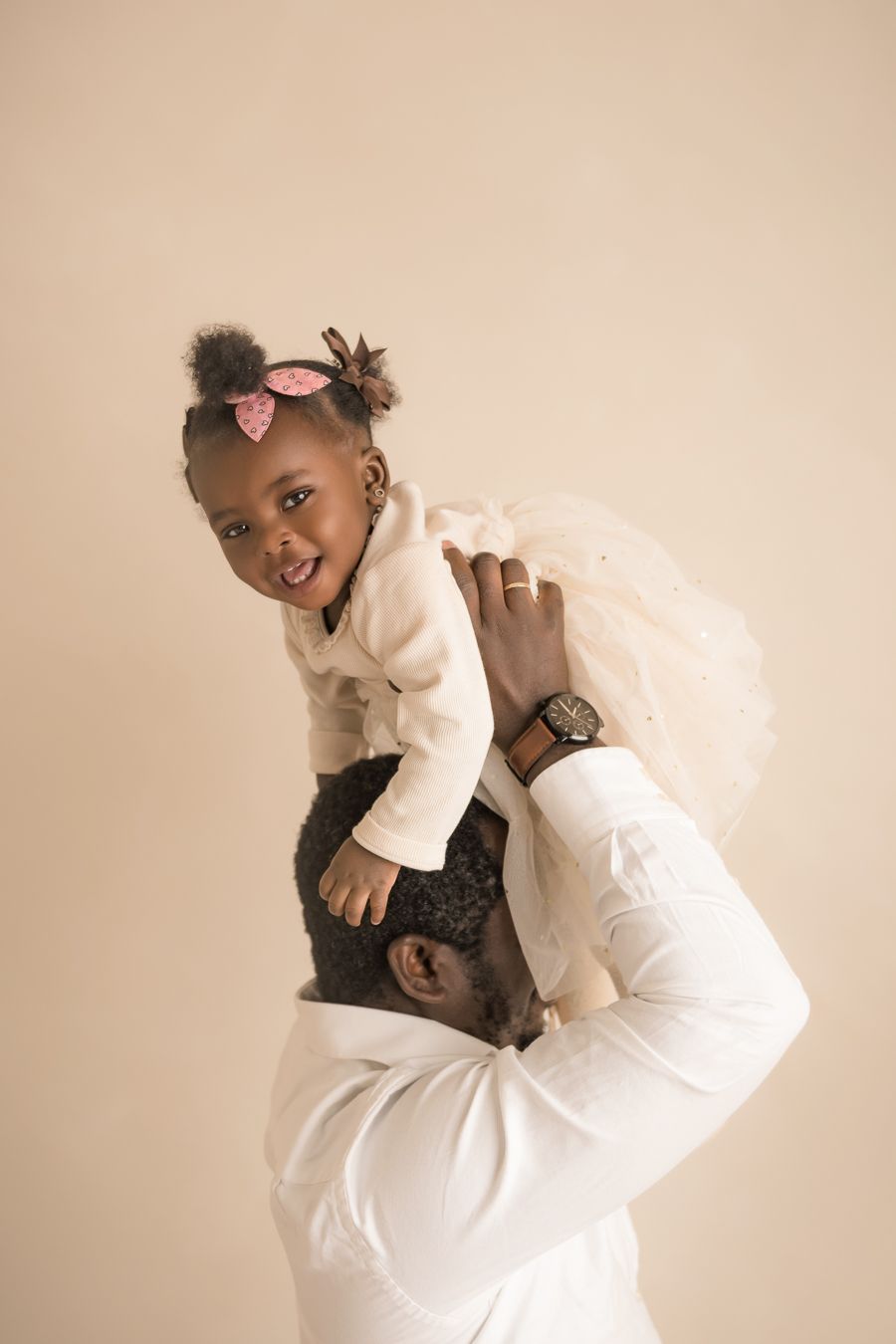 A portrait of a one year old birthday photography session with baby girl laughing on dad's shoulder.