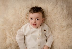 Newborn sibling lies on soft cream-colored fur blanket while smiling at newborn and family photography session.