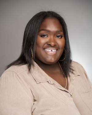 Professional headshot portrait of someone in a beige button-up shirt against a gray background.