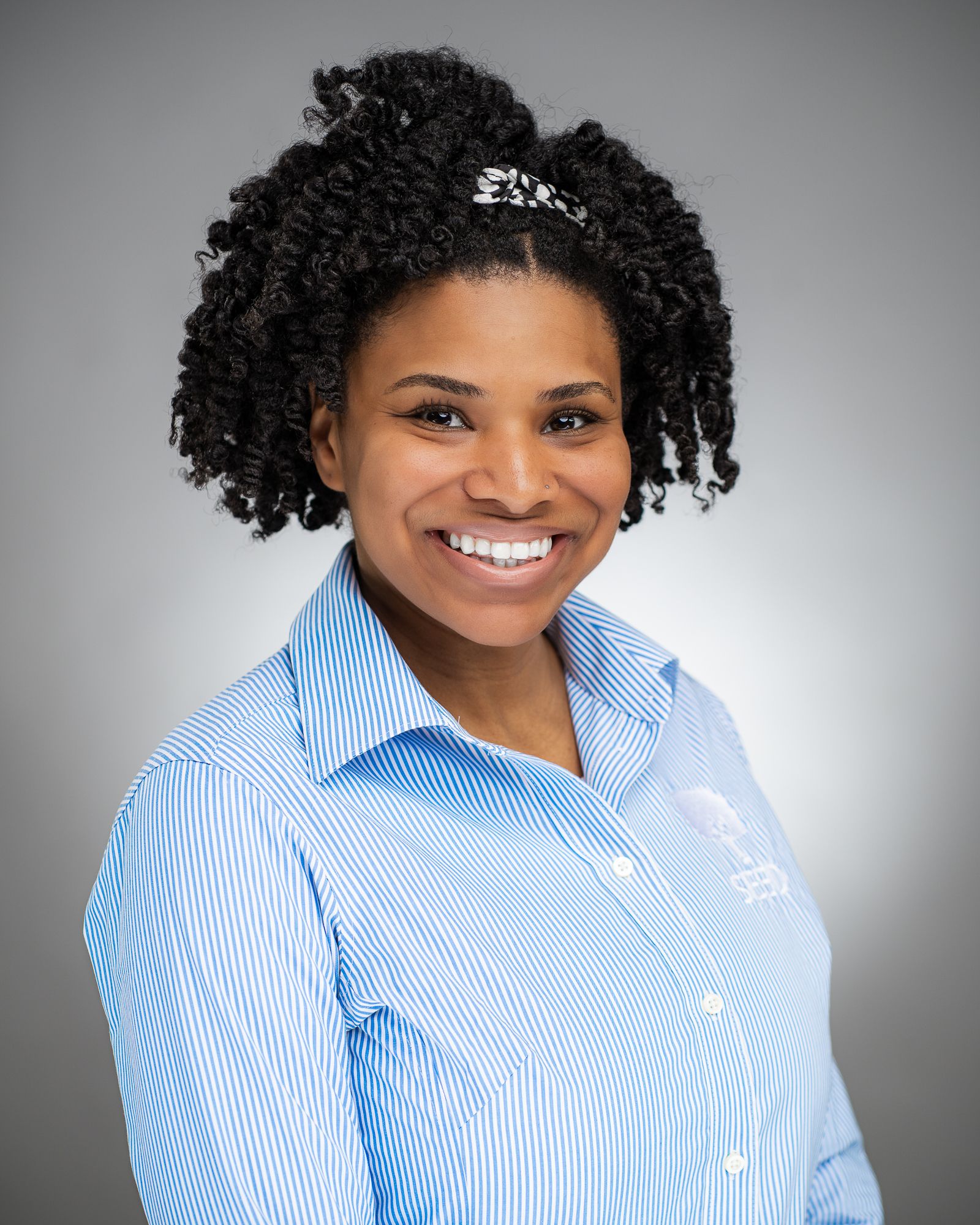 Professional headshot of person in light blue button-down shirt against gray background.