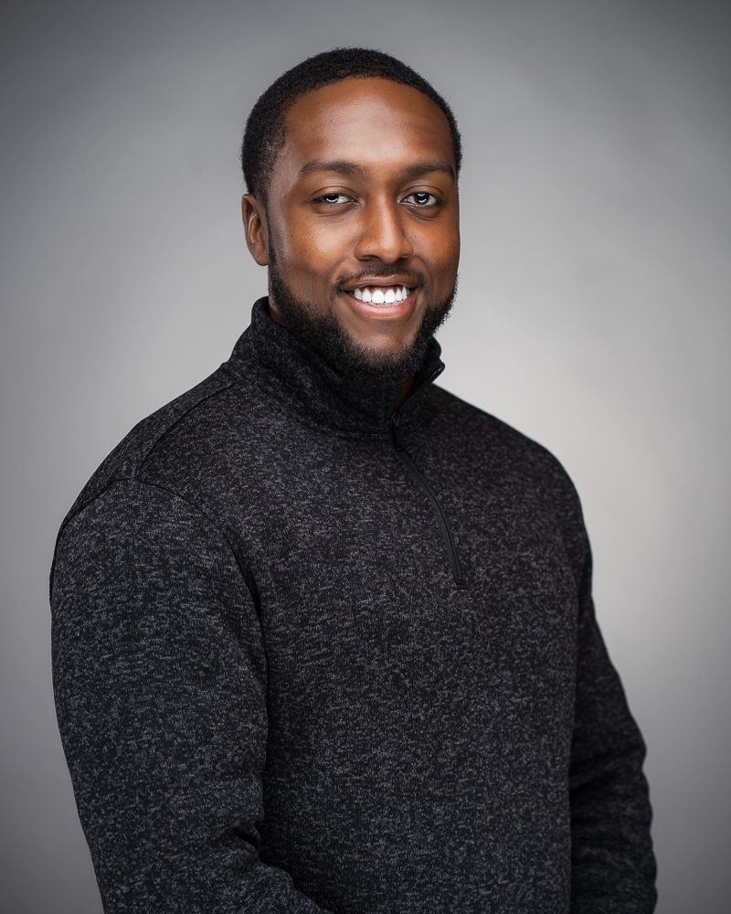 Professional studio portrait with dark turtleneck sweater against gray background.