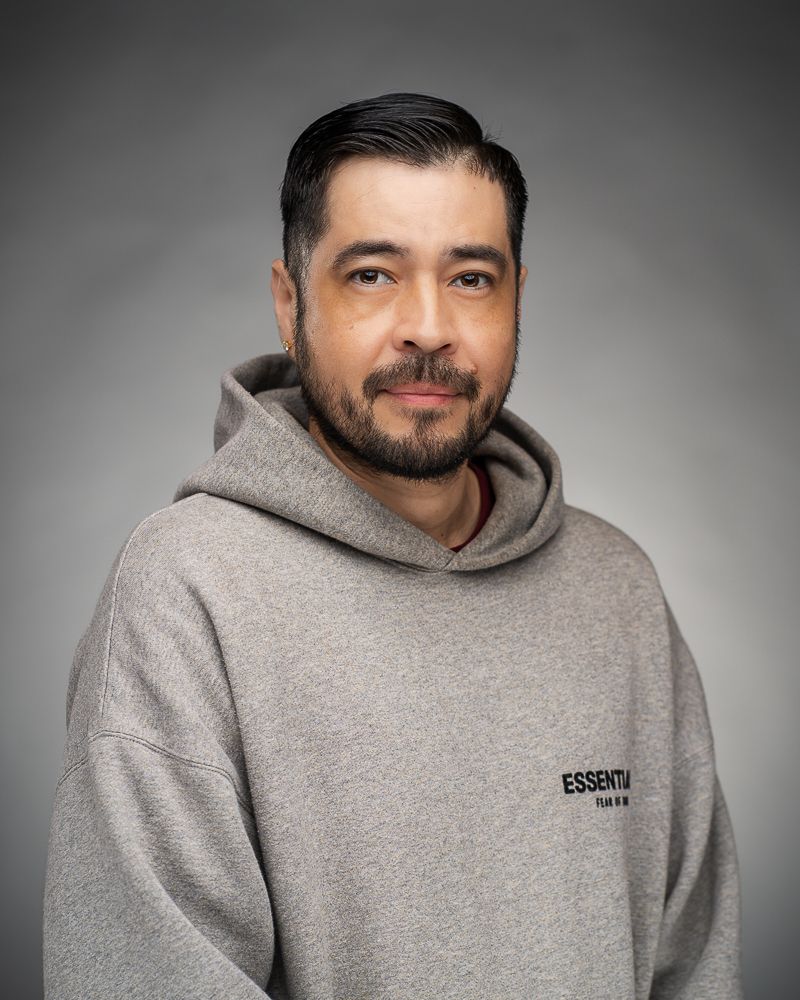 Studio portrait of person in gray hoodie with facial hair against gray background.