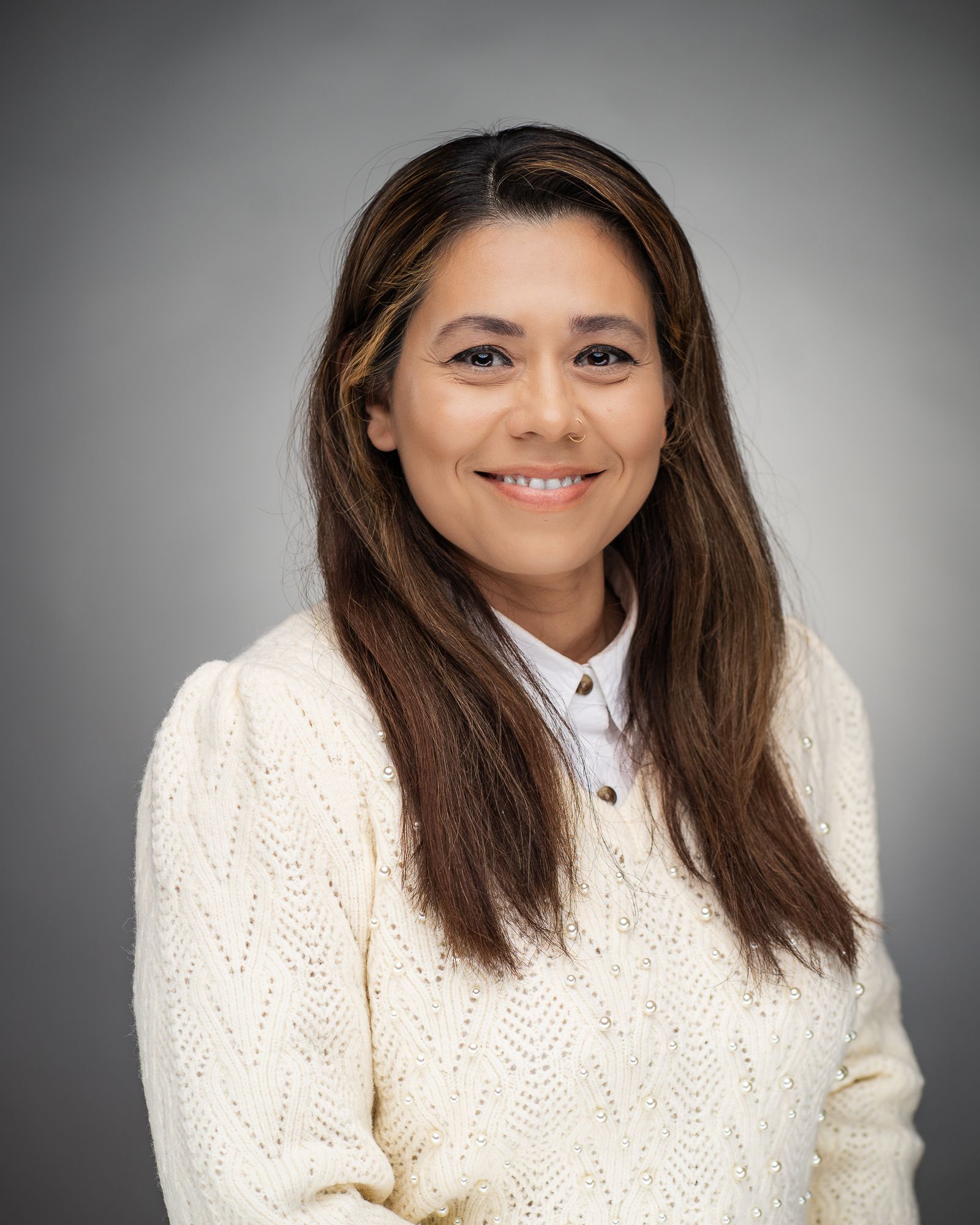Woman in white knit sweater poses for professional headshot against gray background.