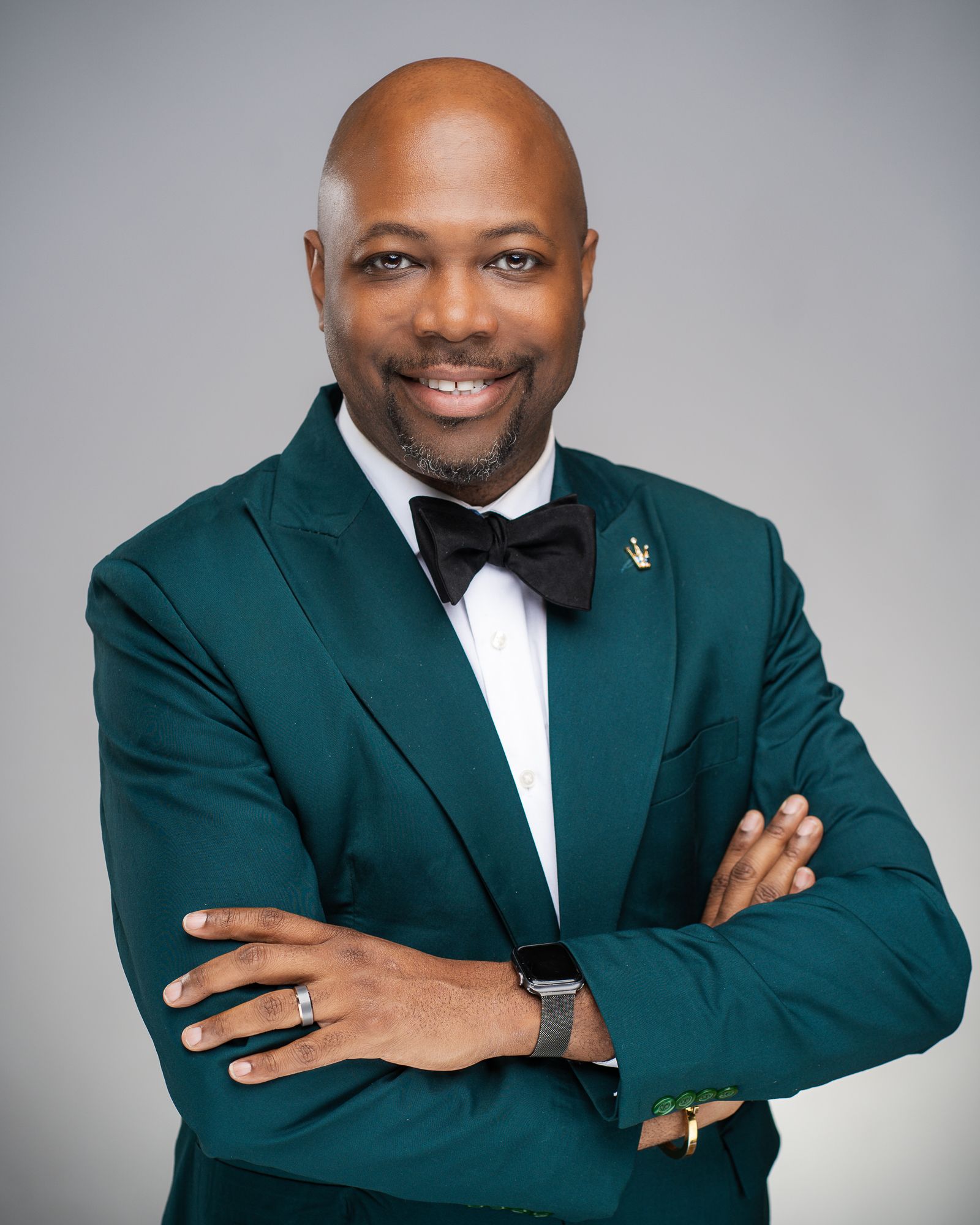 Professional portrait of person in emerald green tuxedo with black bow tie against gray background.