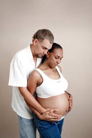 A couple in white shirts embrace tenderly while admiring a pregnant belly in an intimate maternity photoshoot.
