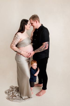 Intimate maternity photo featuring a couple in elegant attire with a small child peeking from behind.