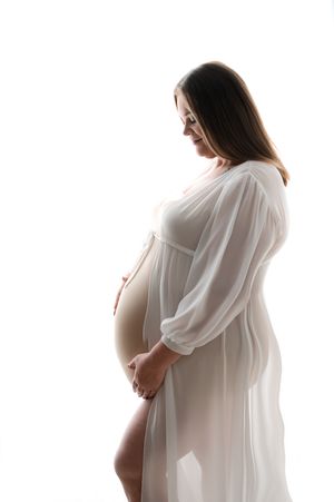 A silhouetted profile of an expectant mother in a flowing white dress poses against a bright background.