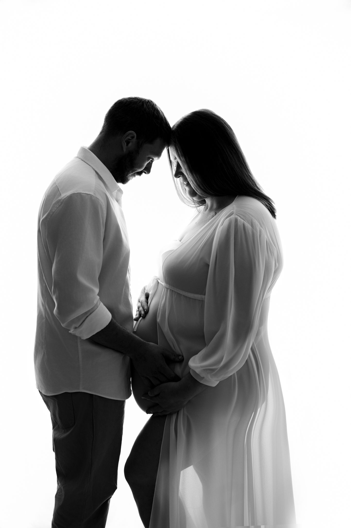 A silhouetted couple shares an intimate maternity moment in a minimalist black and white portrait.