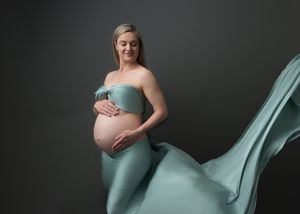 Elegant maternity portrait with flowing seafoam green fabric against dark backdrop.
