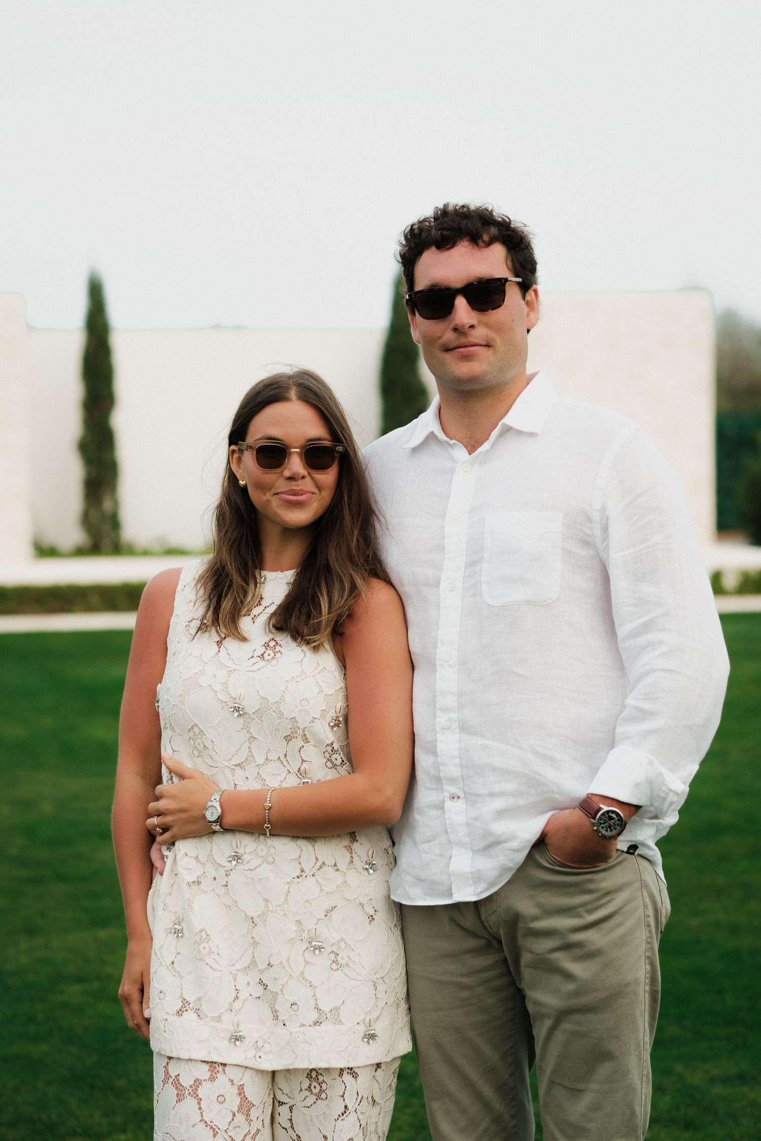Stylish couple in white and khaki posing together on manicured lawn.