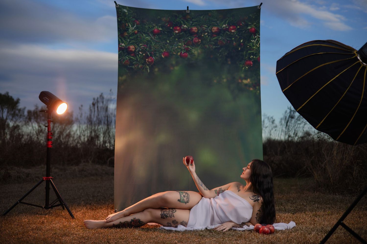 Woman wrapped in white fabric poses in front of a printed orchard backgroundtown, lit by studio lights. Photo by Carolina Waldroff