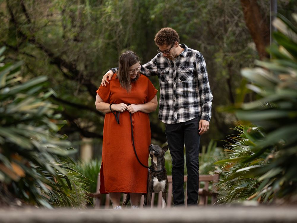 A couple shares a romantic moment together while walking through a lush garden setting with their dog