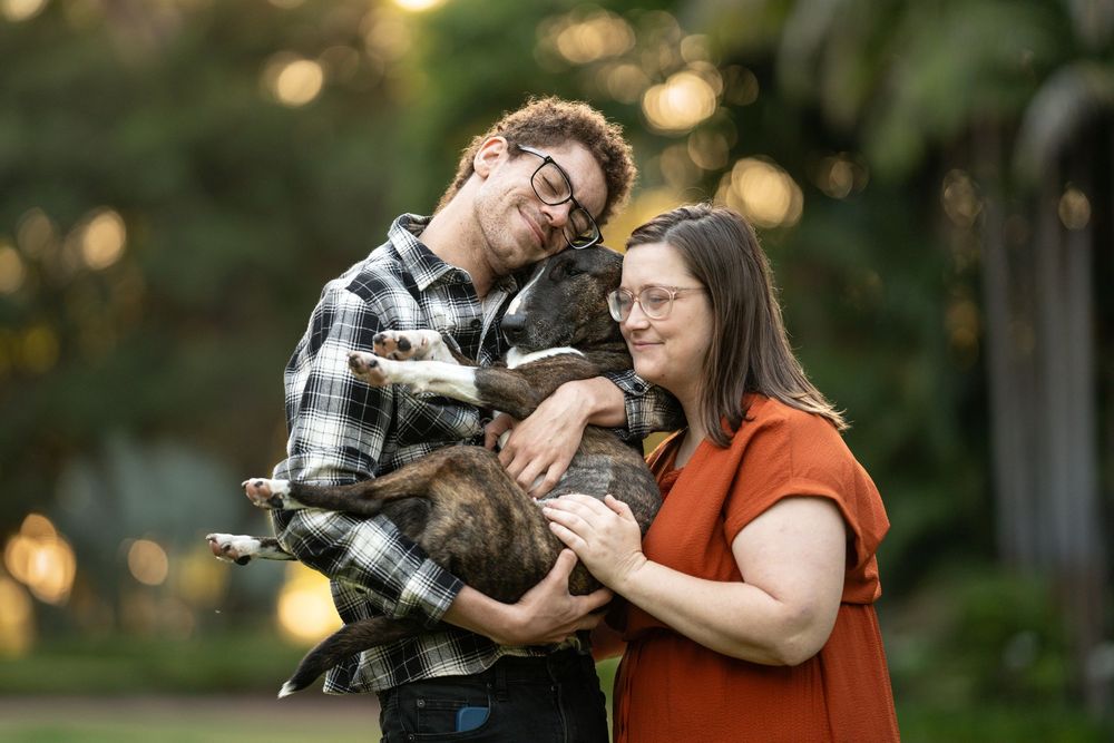 A couple holding and cuddling their dog at their dog photoshoot with bokeh in the background.