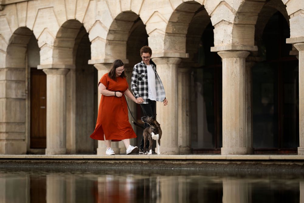 Stone archways line a covered walkway with people walking beneath the columns and arches in an architectural setting.