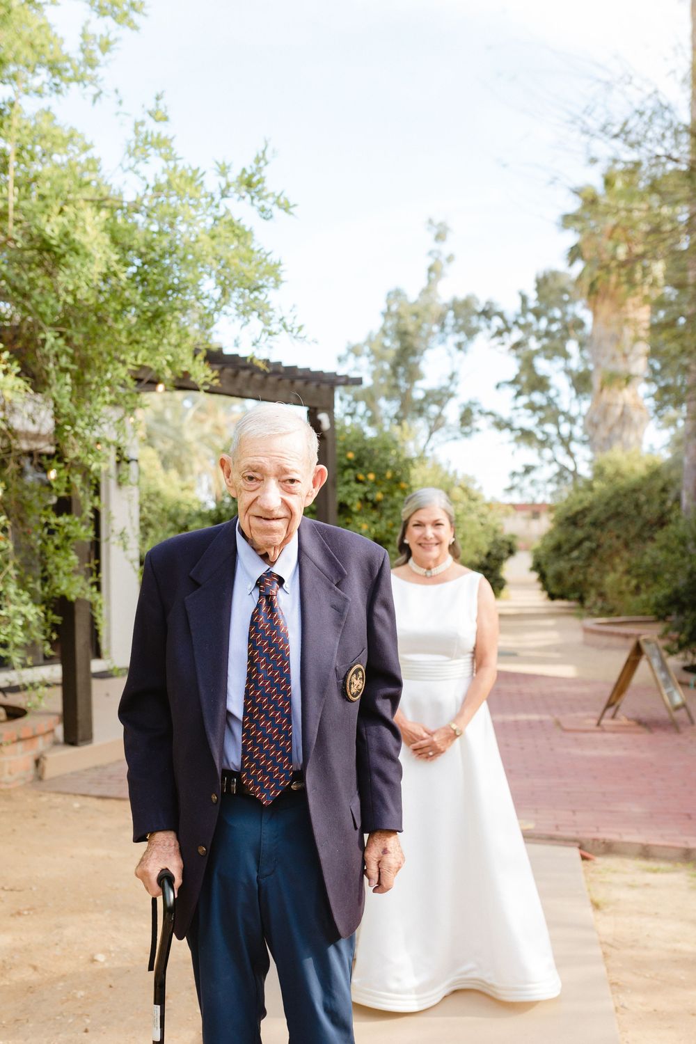 A heartwarming moment before a first look with dadcaptured outdoors with a white wedding dress and formal navy suit along a tree-lined path.