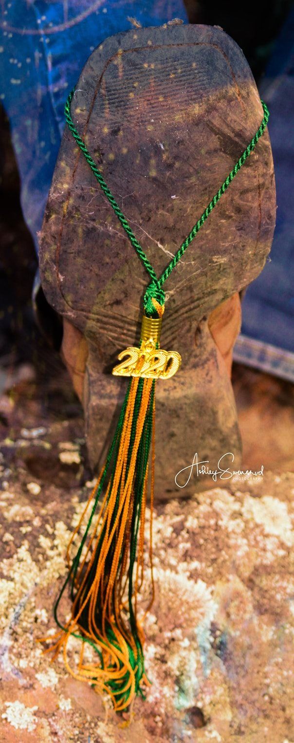 Class of 2020 graduation tassel draped over worn cowboy boot on rocky ground.