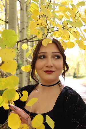 Young woman with dark hair and red lips smiling among bright yellow autumn aspen leaves outdoors.