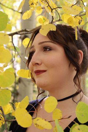 Close-up portrait of brunette woman with red lips framed by vibrant yellow fall aspen leaves.