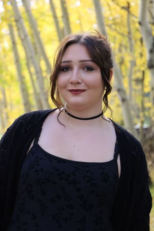 Young woman in black dress and choker necklace posing in front of yellow autumn aspen trees.