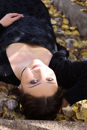 Close-up of woman lying back on stone surface with yellow autumn leaves scattered around her.