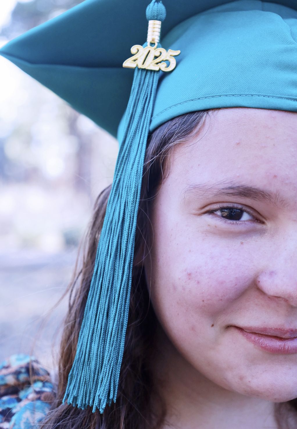 Close-up of a smiling student wearing a teal graduation cap with a 2025 tassel charm.