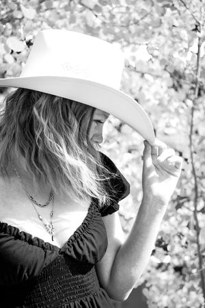 Black and white photo of a woman in a white cowboy hat and black dress among trees.
