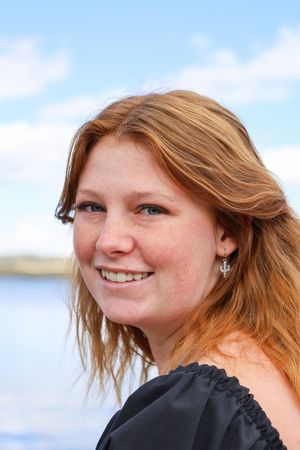 Smiling redhead woman with freckles wearing a black off-shoulder dress near a lake.