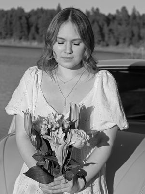 Black and white portrait of a young woman in a white dress holding a bouquet of flowers.