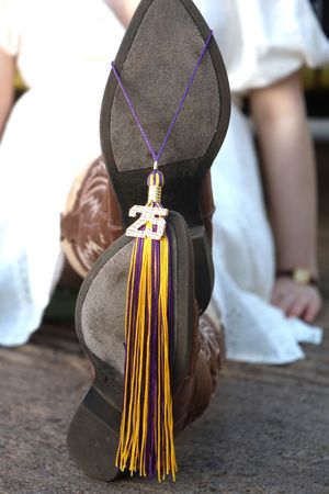 Close-up of cowboy boot sole with gold 2025 graduation tassel in purple and gold colors.