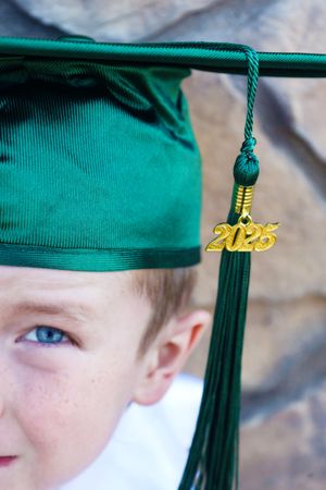 Close-up of green graduation cap with gold 2025 tassel charm on young boys head.