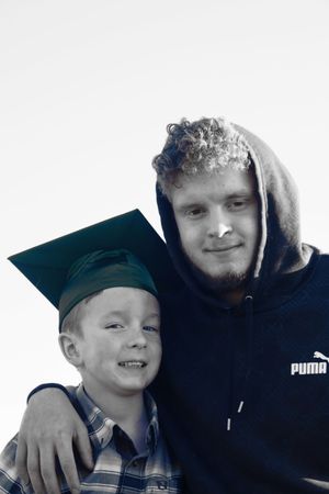Black and white portrait of a young boy in green graduation cap smiling with an older teen.