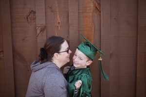Mother and son sharing a joyful smile, boy dressed in green graduation cap and gown outdoors.