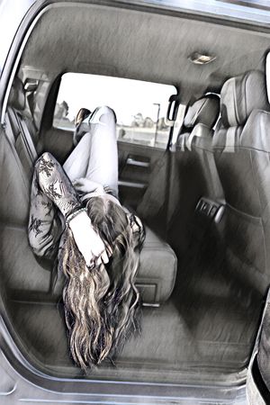 Young woman lying in back seat of SUV, legs up, wearing jeans and black lace top, desaturated edit.