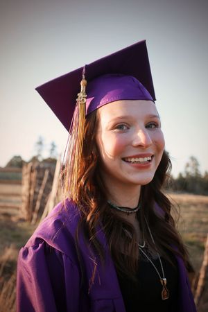 Smiling young woman in purple graduation cap and gown posing outdoors at golden hour.