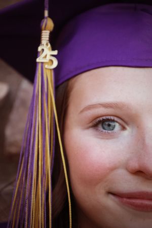 Close-up of graduate in purple cap with gold tassel and 2025 charm, blue eyes visible.