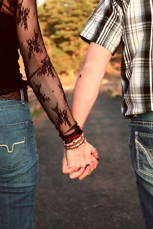 Close-up of couple holding hands, woman wearing black lace sleeve and stacked bracelets outdoors.