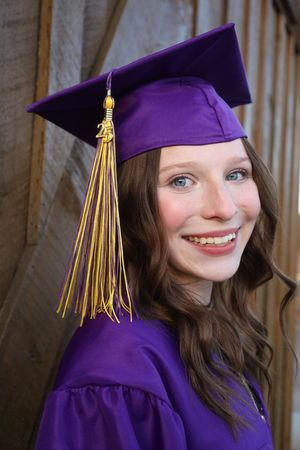 Smiling young woman in purple graduation cap and gown with gold tassel celebrating her achievement.