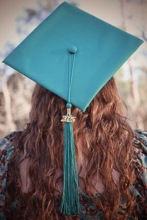 Close-up back view of teal graduation cap with 2025 charm and tassel on curly red hair.