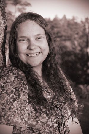 Sepia-toned portrait of a smiling young girl with curly hair leaning against a tree outdoors.