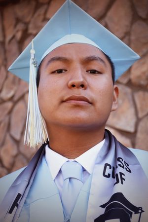 Close-up portrait of young male graduate in light blue cap and gown looking upward confidently.