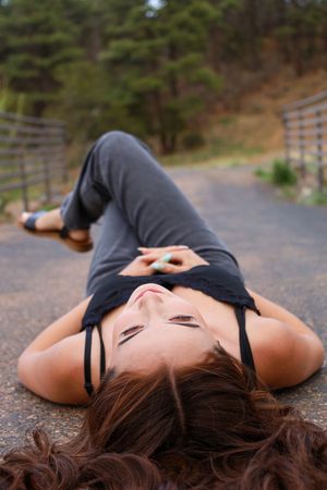 Young woman with long brown hair lying on outdoor path with knees bent looking upward at camera.