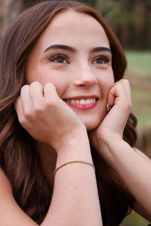 Close-up portrait of smiling young woman with freckles and brown wavy hair holding face in hands.