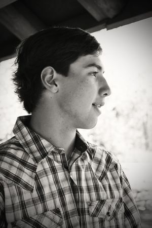 Black and white profile portrait of teenage boy in plaid shirt looking away outdoors.