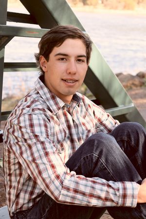 Teenage boy in plaid shirt sitting relaxed on metal stairs outdoors in warm vintage-toned photo.